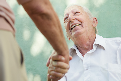 Elderly man smiling and shaking the hand of a man standing in front of him