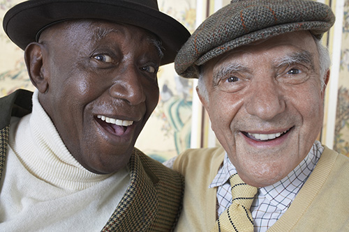 Close up of two gentlemen with big smiles both wearing hats
